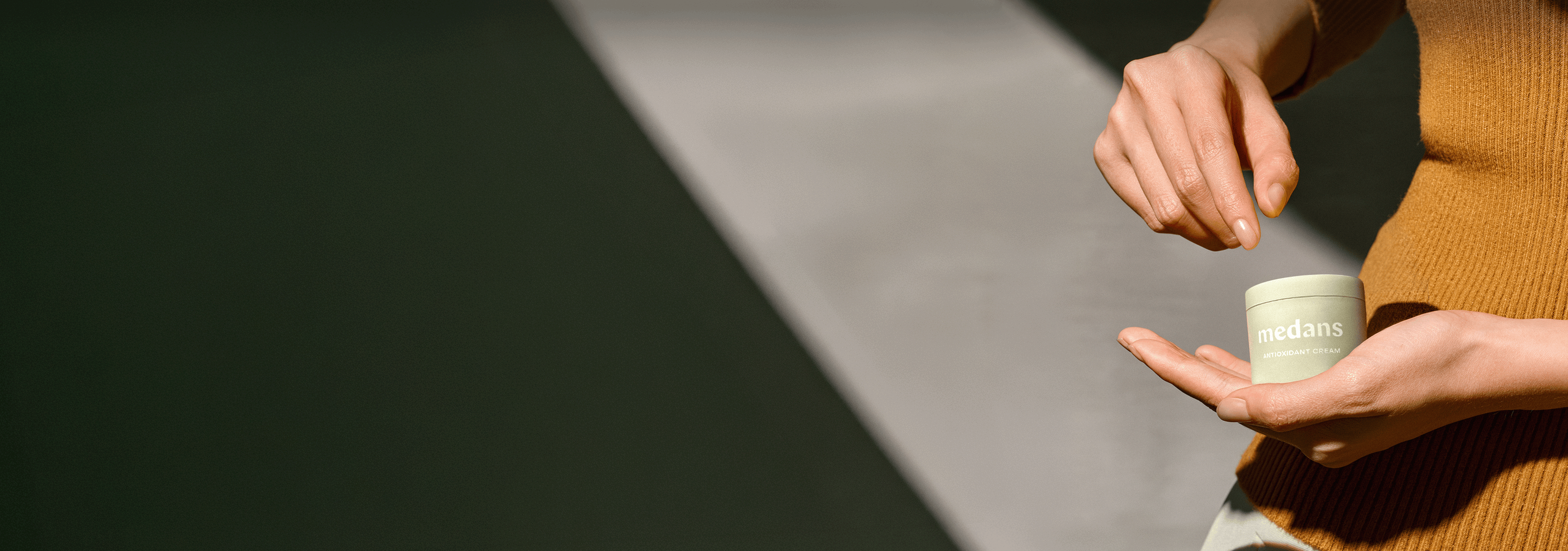 Person holding a container of Medans cream in their palm.